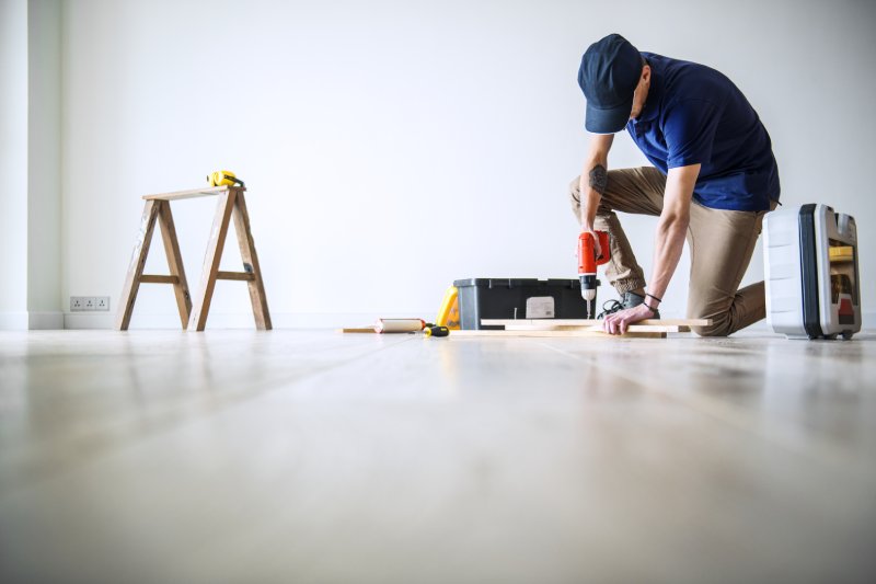 Homeowner making DIY floor repairs with power drill before selling house to increase property value