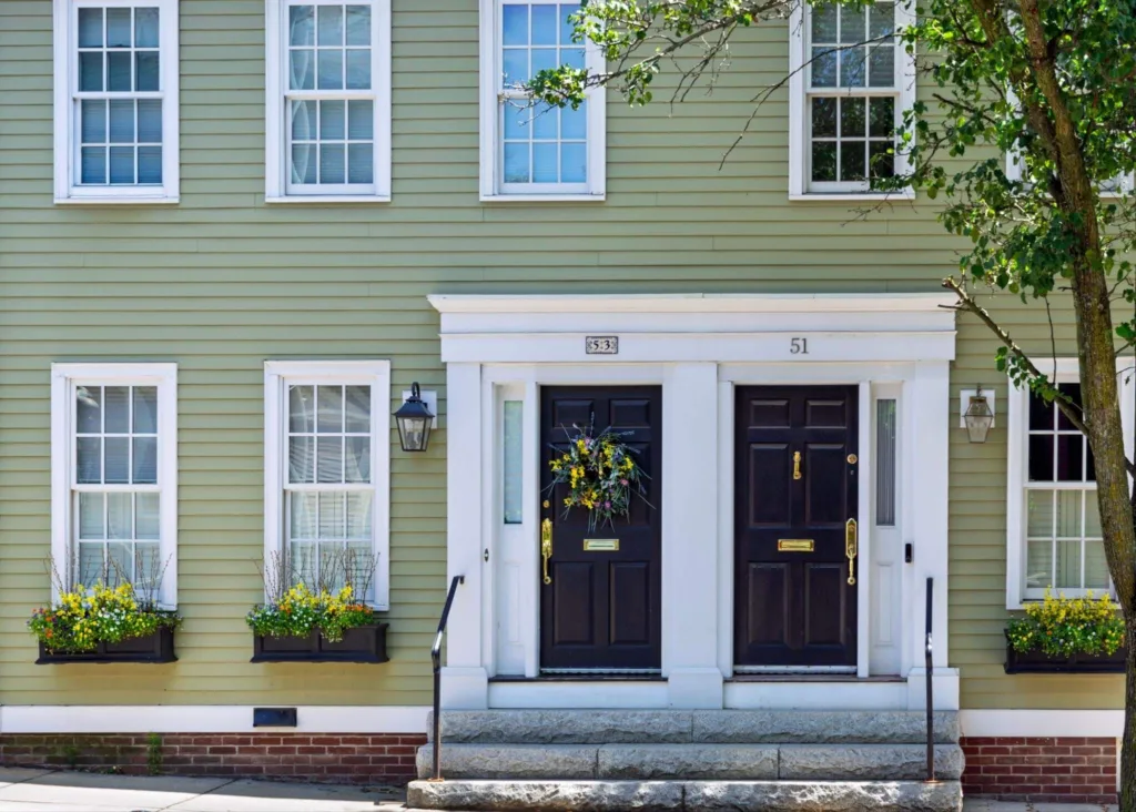 Historic green clapboard house with double black front doors and flower boxes