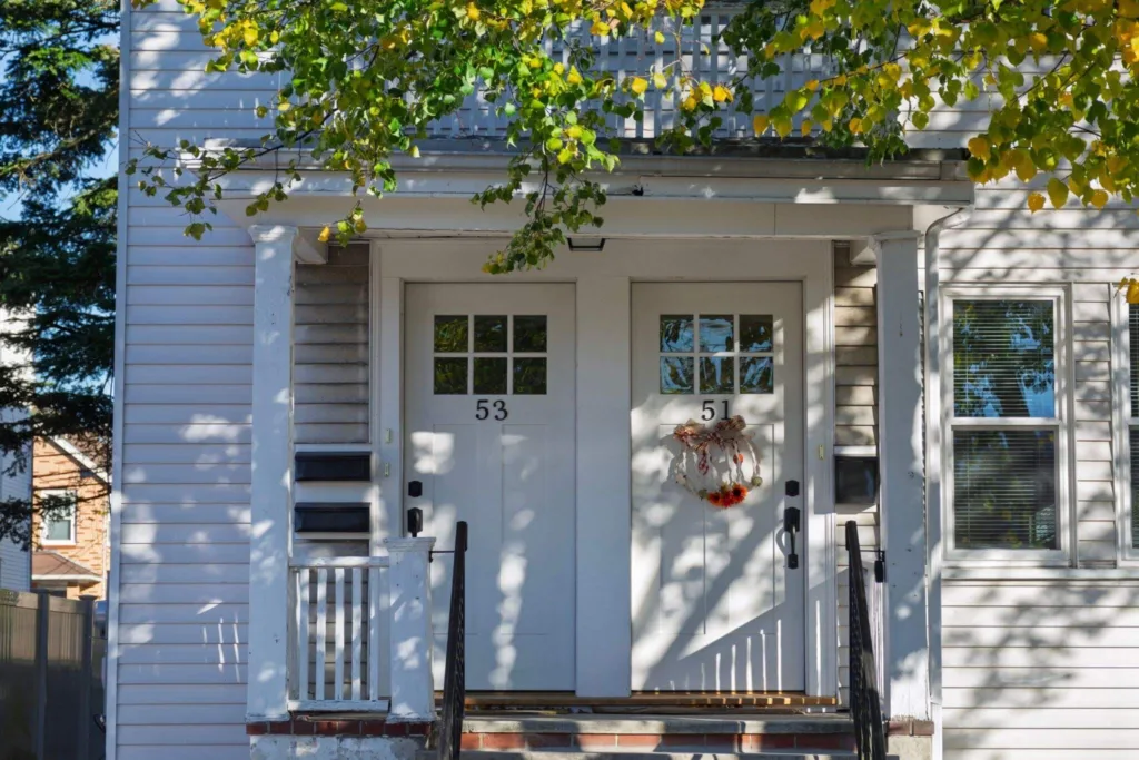 A white duplex house entrance with autumn wreath and dappled sunlight