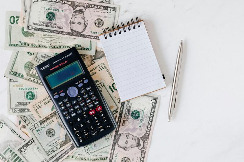 Calculator, notebook, and pen on top of U.S. dollar bills representing real estate calculations, expenses, and financial planning for absorption rate