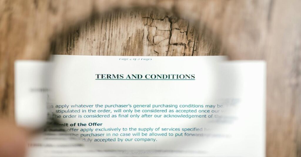 Close-up of a terms and conditions document viewed through a magnifying glass on a wooden table