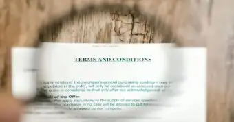 Close-up of a terms and conditions document viewed through a magnifying glass on a wooden table