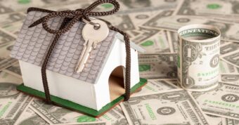 cheapest-way-to-sell-a-house Mini house with key on dollar bills symbolizing home selling costs.