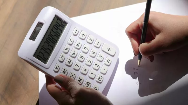 Hand holding a calculator while writing numbers on paper – closing cost calculator