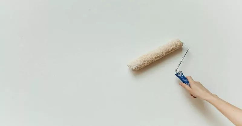 Hand using a paint roller on a white wall, representing home repairs.