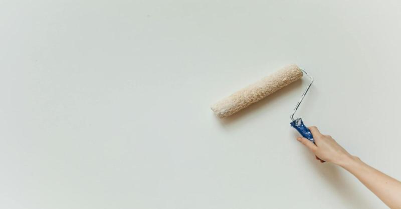 Hand using a paint roller on a white wall, representing home repairs.