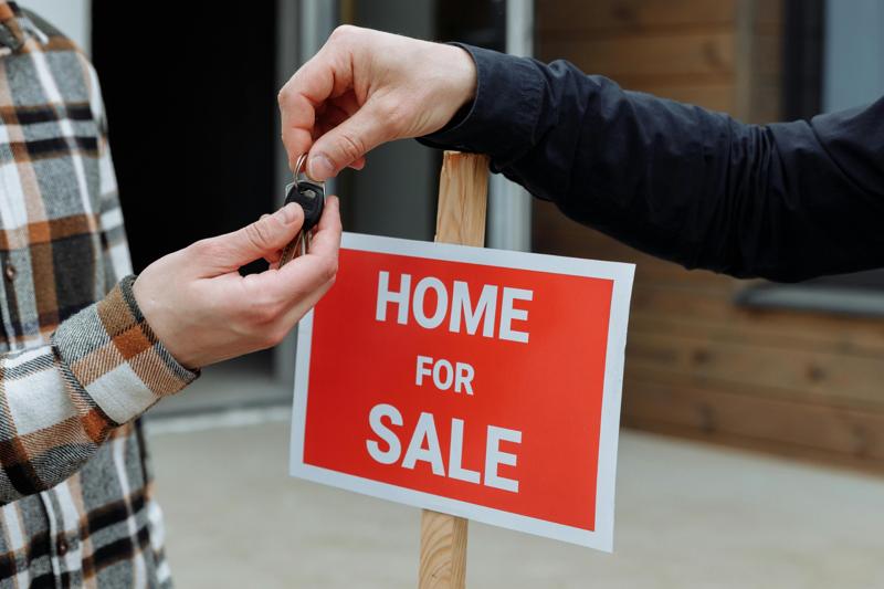 Close-up of a key handoff in front of a home for sale sign