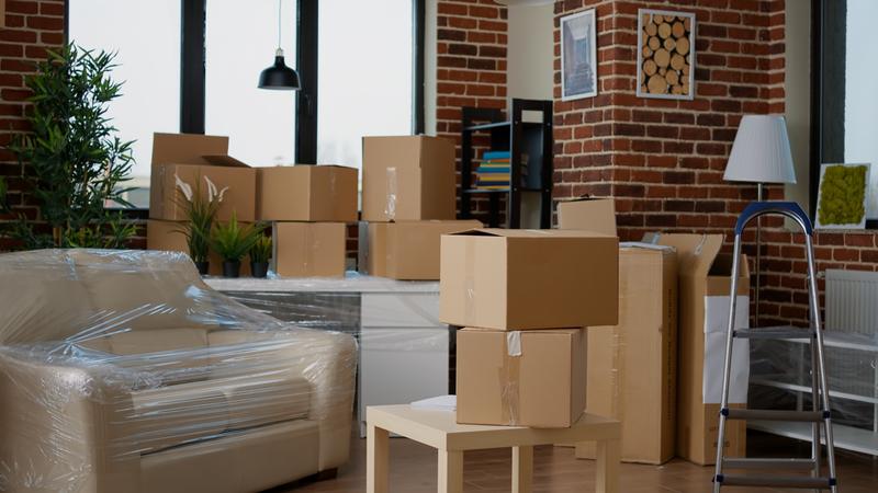 Cardboard boxes packed in a living room with furniture wrapped in plastic.