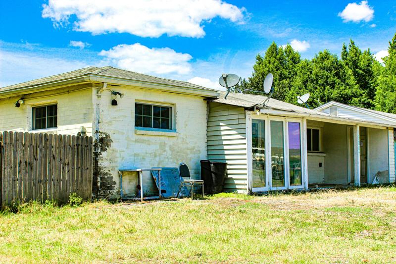 Exterior of an old house with peeling paint and cluttered yard.