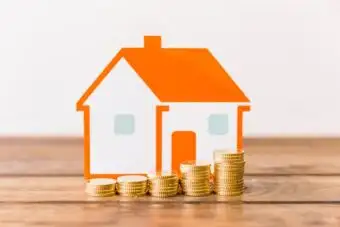 Stacked gold coins in front of house model on desk.
