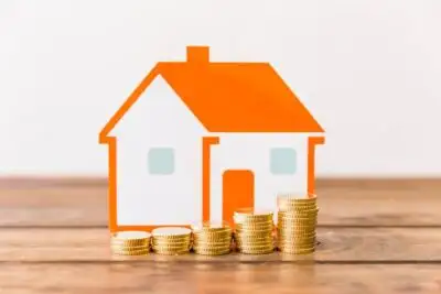Stacked gold coins in front of house model on desk.
