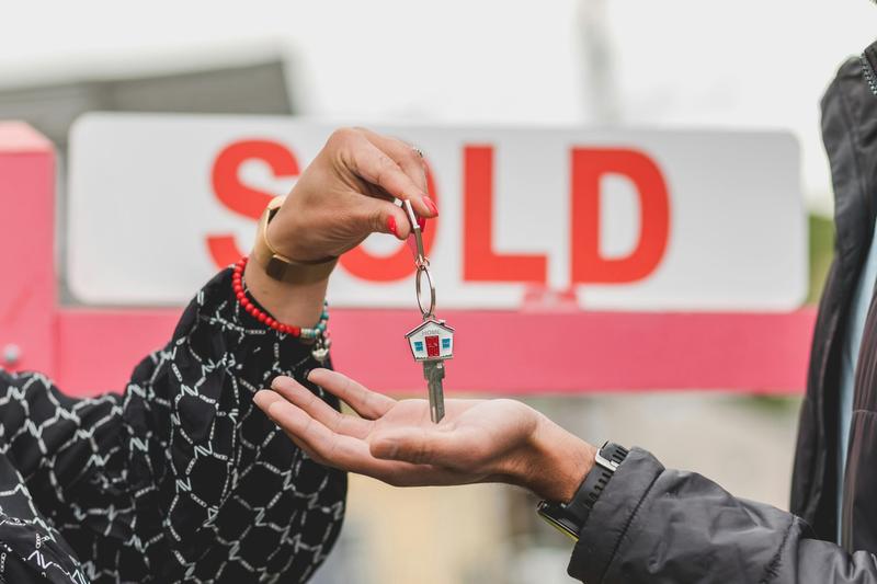 Handing over keys in front of sold sign after inheritance.