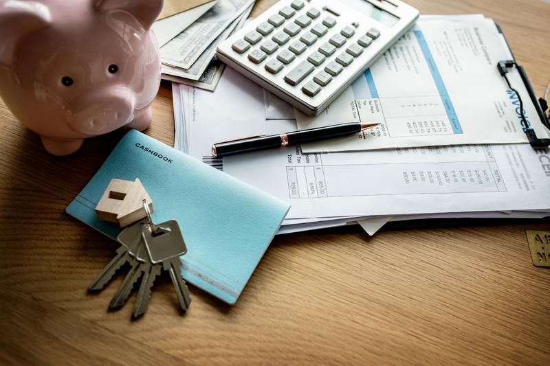 Close-up of financial documents, calculator, pen, piggy bank, and house keys on a desk—representing strategies to save on closing cost.