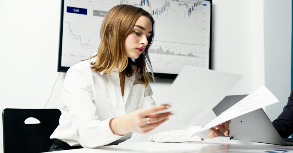 Woman reviewing real estate documents with market graphs in the background.