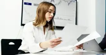 Woman reviewing real estate documents with market graphs in the background.