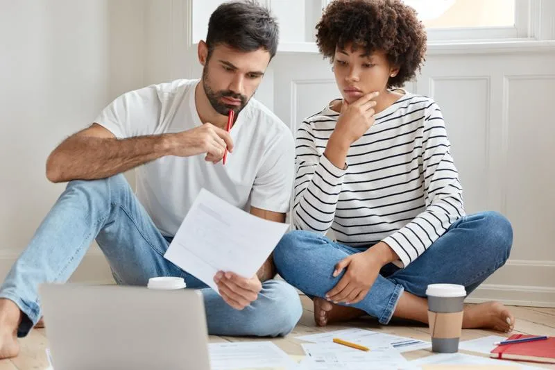 Concerned couple reviewing bills and documents on floor at home.