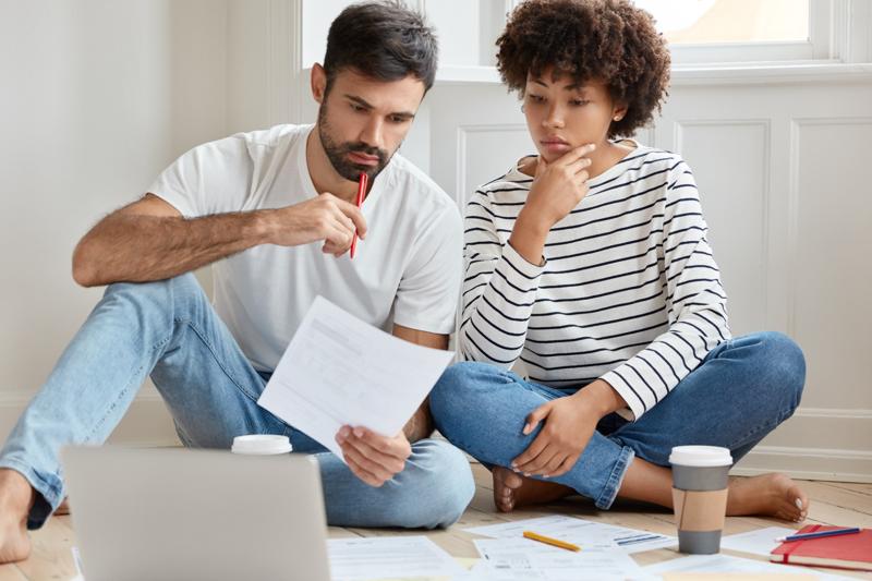 Concerned couple reviewing bills and documents on floor at home.
