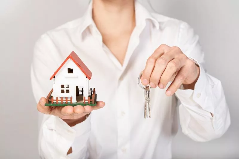 Woman in white shirt holding house model and keys