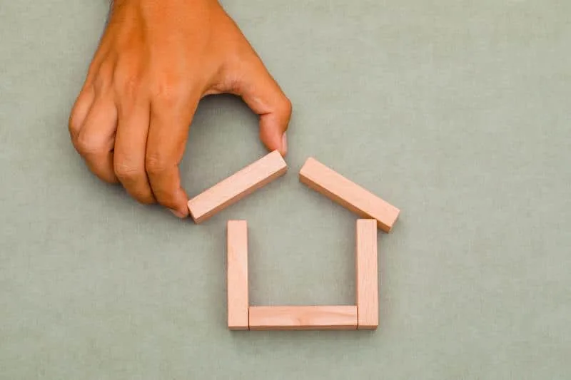 Hand placing wooden block on toy house roof structure