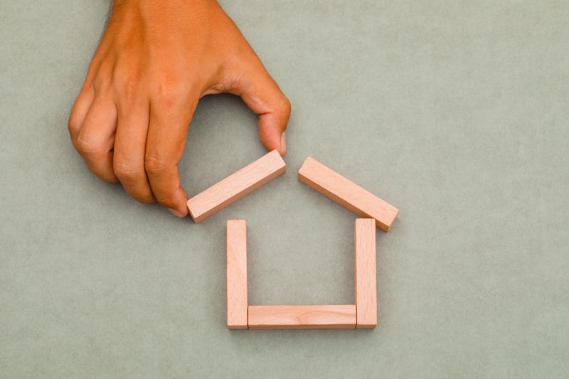 Hand placing wooden block on toy house roof structure