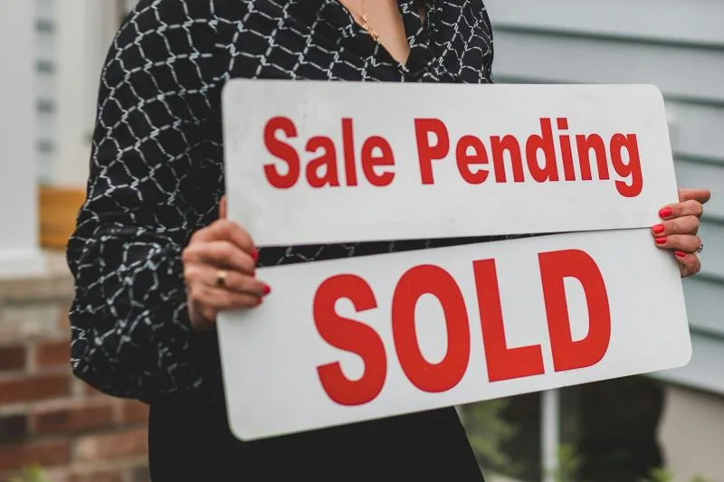 Woman holding a sale pending and sold sign outside a house