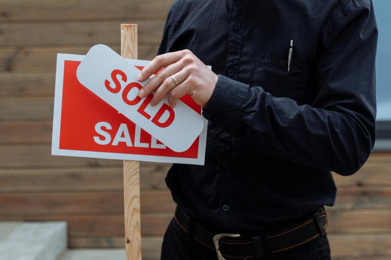 Hand placing SOLD sign over FOR SALE outside a home