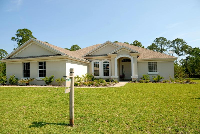 White house with for sale sign and bright green lawn