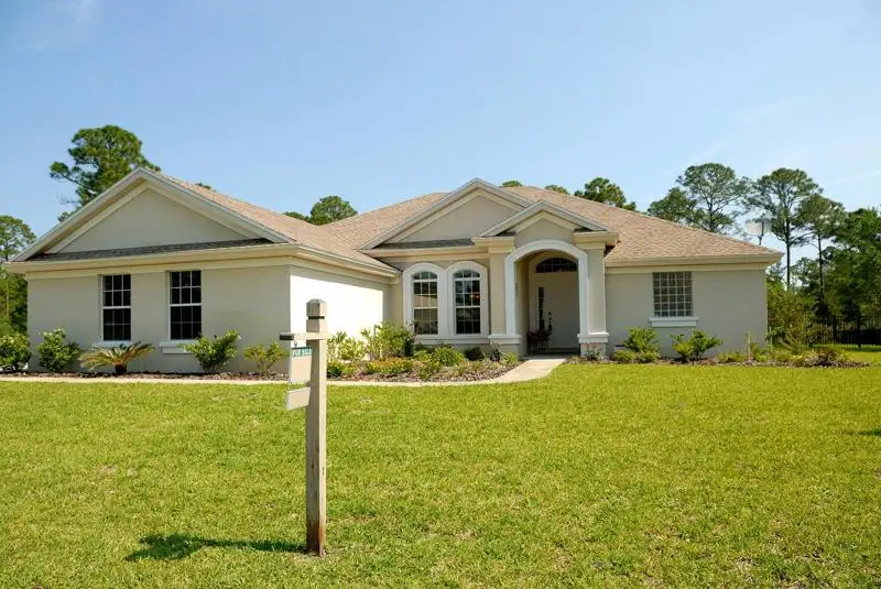 White house with for sale sign and bright green lawn