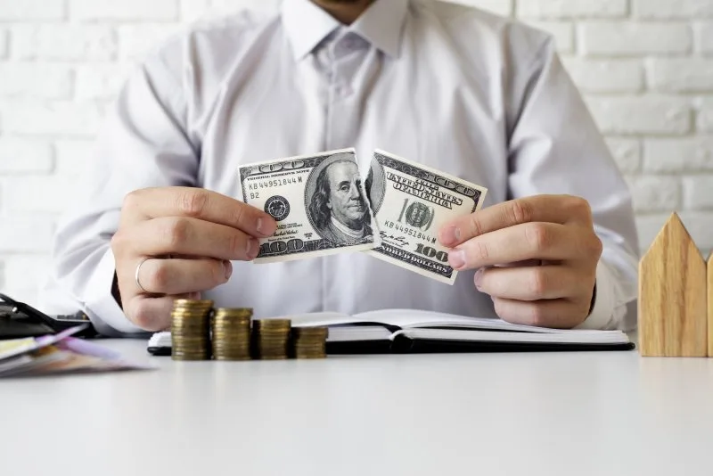 Person tearing a dollar bill symbolizes commission costs in real estate.