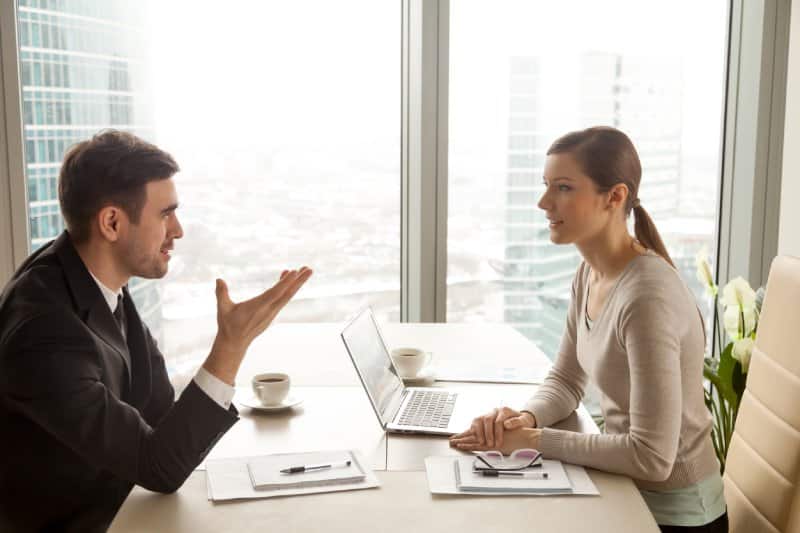 Man and woman discussing house sale options in office meeting.