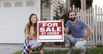 Smiling couple kneeling with For Sale By Owner sign