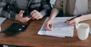 Couple reviewing tax documents with calculator and smartphone in hand.