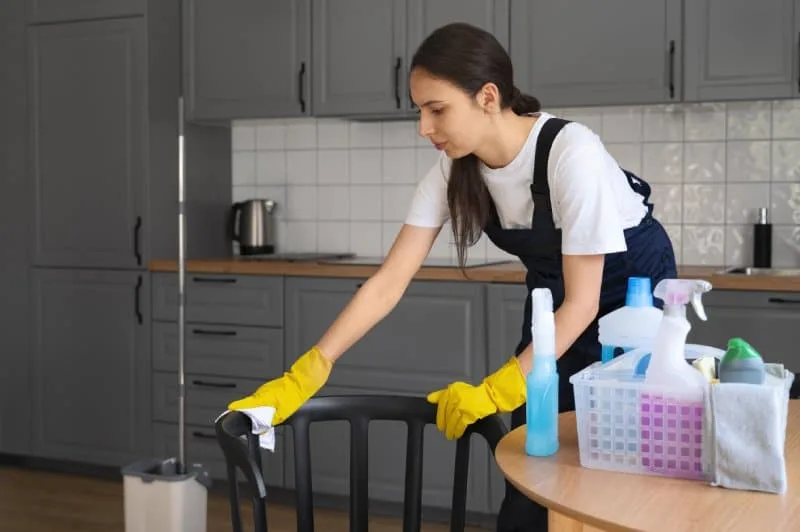 Woman cleaning kitchen chair wearing gloves, preparing house to sell.