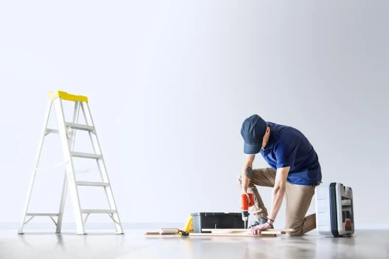 Man using a power drill on the floor, making small home repairs.   