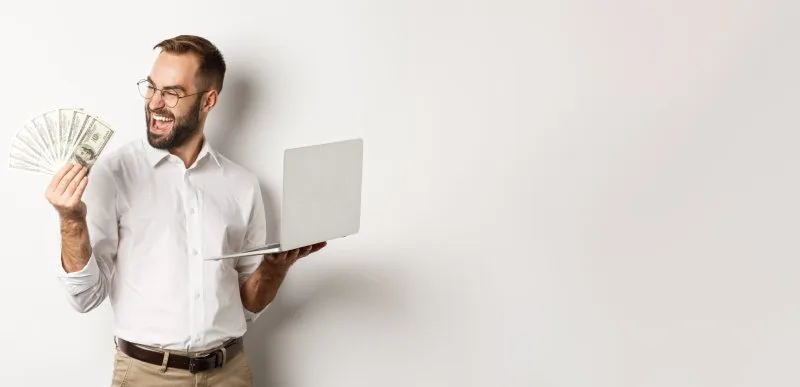 Happy man holding cash and laptop, celebrating home sale.