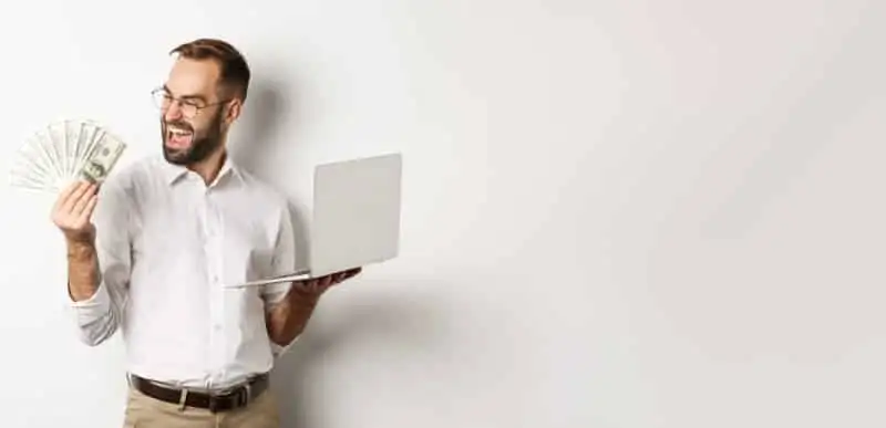 Happy man holding cash and laptop, celebrating home sale.
