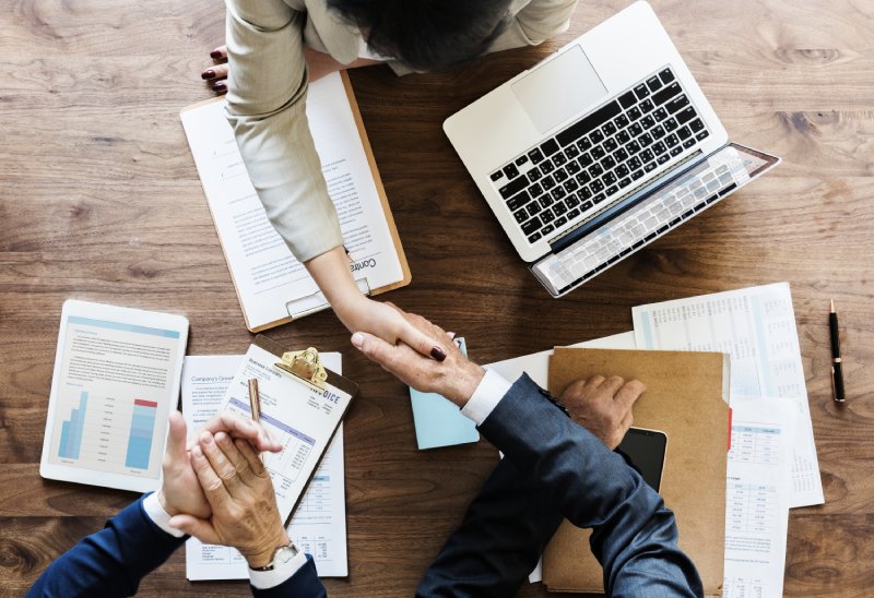 Handshake over contracts and laptop during home sale agreement.