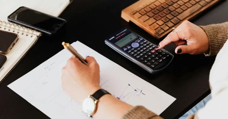 Person calculating California home closing costs with pen and calculator.