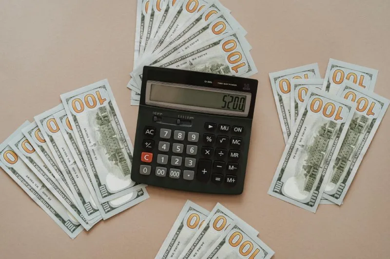 Stacked $100 bills and calculator displaying closing cost amount.