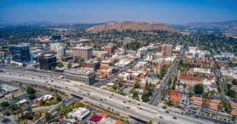 Aerial view of Riverside city with downtown buildings, freeway, and hills, showcasing regional California real estate market.