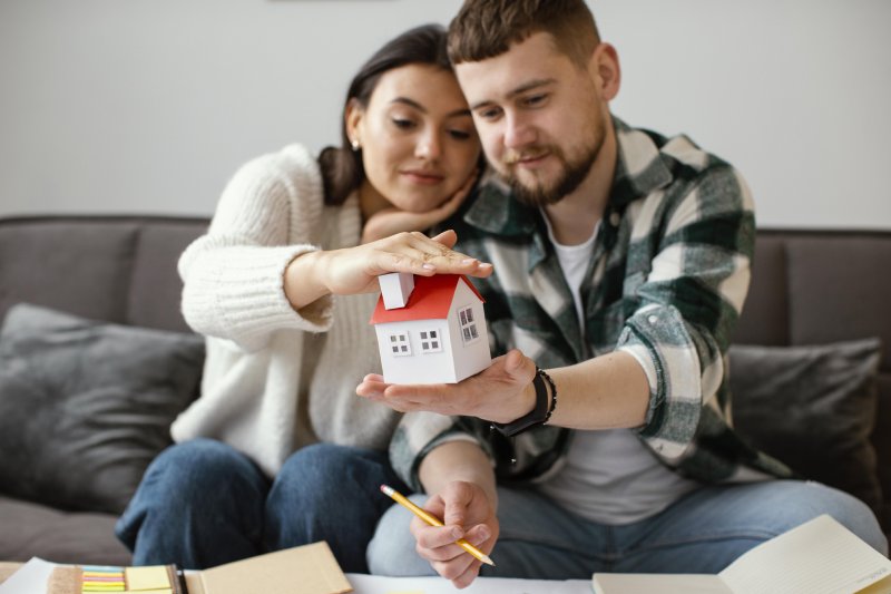 Young couple holding a miniature house model while reviewing trust documents for inherited California property